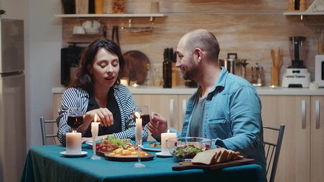 Young married couple having funny moments at dinner. Wife and husband during romantic dinner in the kitchen, dining together at home, enjoying the meal, celebrating their anniversary, surprise holiday