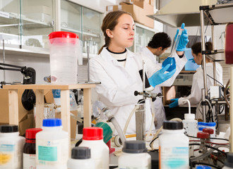 Professional female chemist working in laboratory, analyzing liquid samples in test flasks..