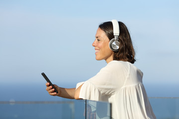 Happy adult woman with headphones listens music on the beach