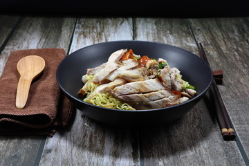Traditional egg noodle topping with roasted duck meat and crispy pork on the dark bowl. Famous Chinese street food menu in Asia. Comfort food concept. 