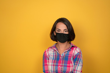 Serious young woman wearing protective mask while looking at camera. Caucasian girl in casual isolated on yellow background. Pandemic concept.