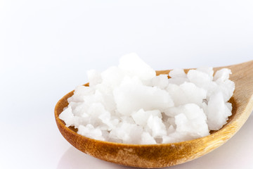 White scrub salt on a wooden spoon against a white backdrop.