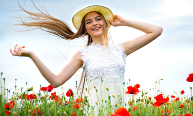 teenage girl standing in a field with wild poppies in a hat looking into the distance