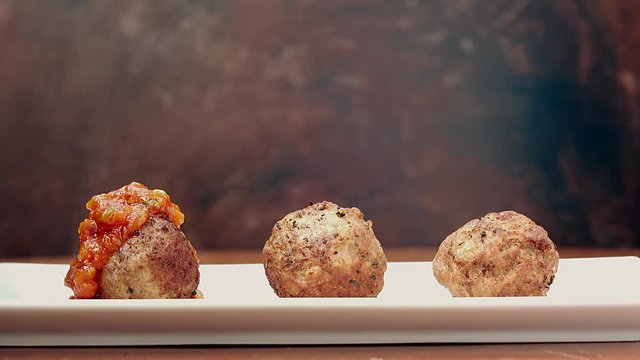 cook puts tomato sauce on three meatballs