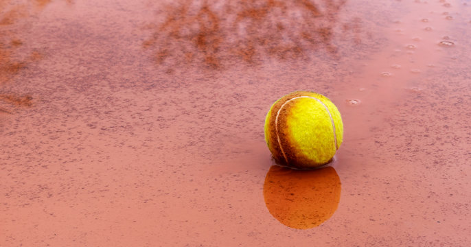 Wet Tennis Ball In Puddle On Outdoor Clay Tennis Court In Rainy Weather. Cancellation Of Match Or End Of Season For Outdoor Sports. Panoramic Size. Banner. Copy Space