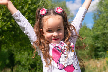 Portrait of a cute beautyful smiling little girl with hands up in a summer park, close-up. Childhood concept