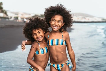 Happy sisters enjoying inside sea water during summer time - Afro kids having fun playing on the...