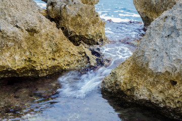 Sea tide breaking between coastline stones from raging sea to calm bay. Wave is blurred