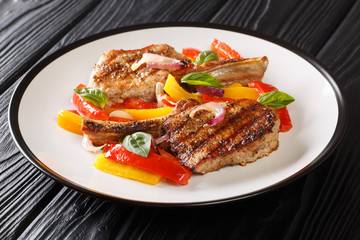 Delicious grilled pork chop with bell peppers, onions and basil close-up in a plate on the table. horizontal