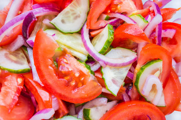 Close up view onto salad made from garden vegetables, such as tomatoes, cucumbers & red onion, mixed & seasoned with olive oil