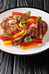 Grilled spicy pork chop with stewed yellow and red bell peppers and onions close-up in a plate on the table. vertical