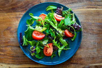 Simple salad of mixed greens and tomato on rustic wooden board, flat lay