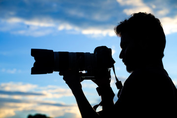 Silhouette of a man photographer with dslr camera during taking photos at sunset