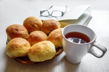 Cup of tea & wooden plate with home baking. Blurred glasses & book are on background