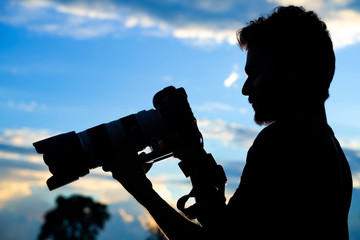 Silhouette of a man photographer with dslr camera during taking photos at sunset
