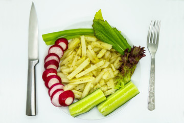 Fried potatoes with spices, chopped radish, cucumbers, green onions, lettuce. Knife and fork lying nearby