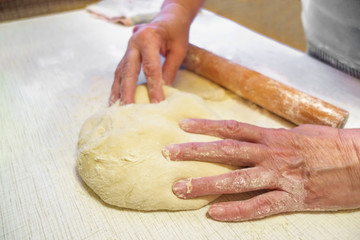 Woman manually prepares dough for pizza or pie. The rolling pin lies in the background