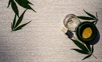 Cosmetic mask in a jar, pipette, serum capsules on a stand, plant leaves on a light background....