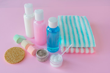 Cosmetics for cleansing the skin of the face. Lotion, scrub, cream, wash gel, sponge and towels on pink wooden background. Concept of daily skin care, cleansing, spa