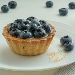 Blueberry tartlets served on a white plate with brown sugar. Glass of milk in the sun on a white background.