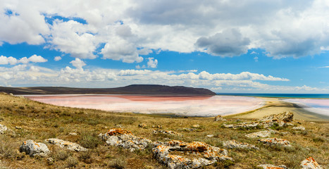 Landscape. View of a small pink lake from the mountain. In the foreground are huge old stones. above the lake blue sky with clouds.