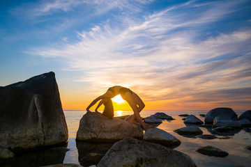 Anonymous female bending back on stones near sea
