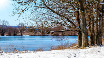 Winter landscape with forest over the river in sunny weather