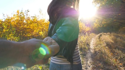 Young woman holds male hand and jogs along path near woodland. Follow me shot of happy girl leads her boyfriend along trail near autumn forest. Beautiful nature at background. Concept of loving. POV - Powered by Adobe