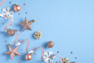 Christmas background with rose gold color decorations, balls, stars, glittering confetti on blue table. Flat lay design, top view. Xmas, winter holidays, New Year greeting card template.