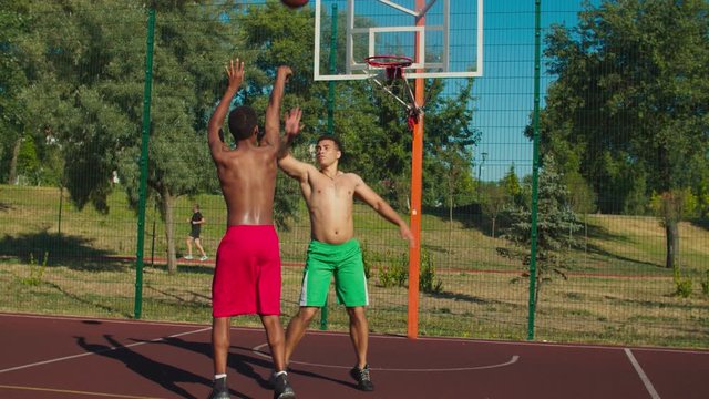 Two positive shirtless muscular build multiethnic basketball players exchanging friendly handshake on outdoor urban court after streetball match, expressing good sportsmanship, respect and fair play.