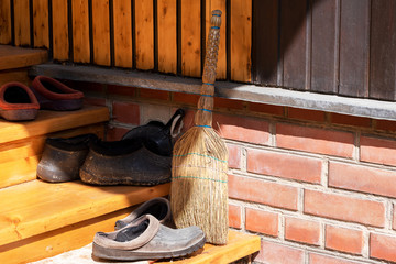 Broom and garden shoes on the threshold of a rural house in the rays of the bright sun