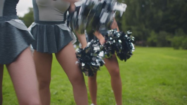Cropped shot of cheerleading team in uniform performing dancing element with pompons