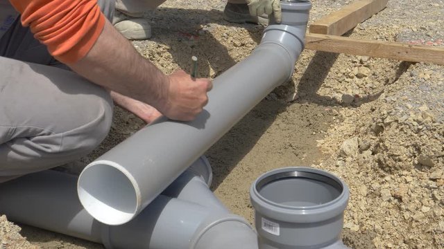 SLOW MOTION, CLOSE UP: Unrecognizable builder marks a plastic sewage pipe with a pencil. Close up shot of a contractor's hands as he marks a line on a plastic pipe while assembling a sewage pipeline.
