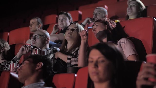 Cheerful groups, couples of audience enjoying free time in movie theater. Joyful spectators chatting, relaxing, eating popcorn, drinking soda while watching film in cinema hall