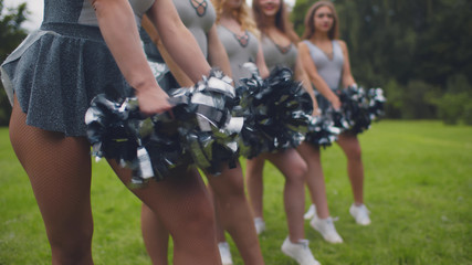 Cropped shot of cheerleading team in uniform performing dancing element with pompons - obrazy, fototapety, plakaty