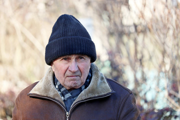 Portrait of unhappy elderly man standing outdoor. Concept of cold weather, life in village, old age