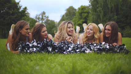 Portrait of five smiling cheerleading girls lying on grass in park and chatting