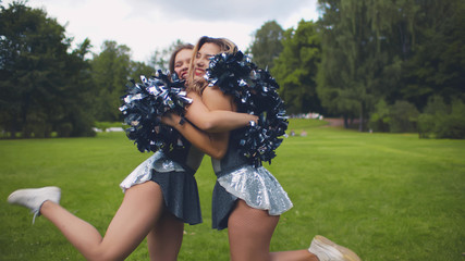 Portrait of happy cheerleaders with pompons hugging standing in park