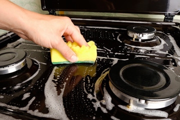 woman cleans gas stove with a washcloth and foam, surface cleaning, cleaning the kitchen, kitchen appliances