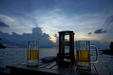 Cold beer and summer sunset on beach with blurred landscape of sea