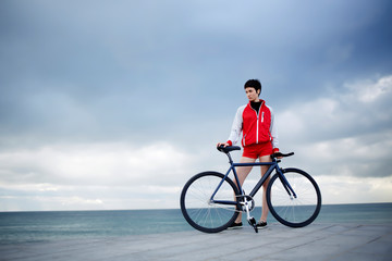 Attractive hipster girl relaxing on the beach after ride on her sport fixed gear bicycle,young woman at seashore enjoying her recreation time outdoors, female with rental bike enjoying weekend stroll
