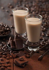 Shot glasses of Irish cream baileys liqueur with coffee beans and powder with dark chocolate on dark wood background.