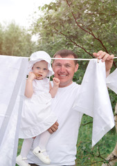 Happy father with his little daughter hangs white linen in the village in the outdoor