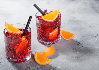 Negroni cocktail in crystal glasses with orange slice and black straw on light background.