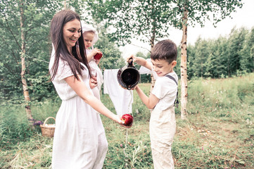 Happy young mother in a white retro dress in the village washes a red apple with her little son outdoor