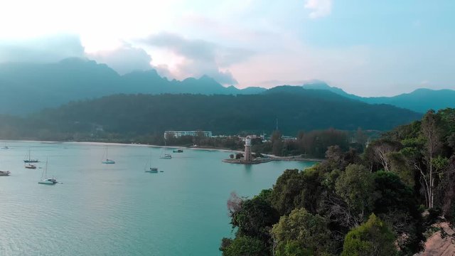 Drone shooting. Aerial photography. The drone flies over the bay of a tropical island with a lighthouse tower. Perfect turquoise water, mountains in the background. Tropical landscape