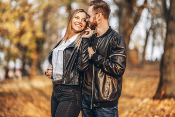 Beautiful young couple walking in the autumn park on a sunny day. They hug and smile, enjoy a walk