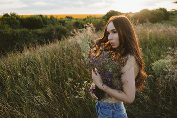 National Relaxation Day, relaxation practices, mental health, slow living concept. Young girl with long windy hair and flower bouquet enjoying nature on the background of sunset