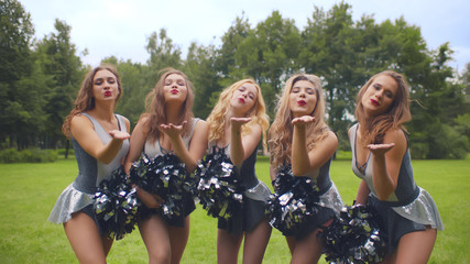 Girls cheerleaders with pompons blowing kisses smiling at camera