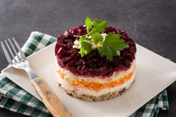 Traditional Russian herring salad with beetroot and carrots on black background